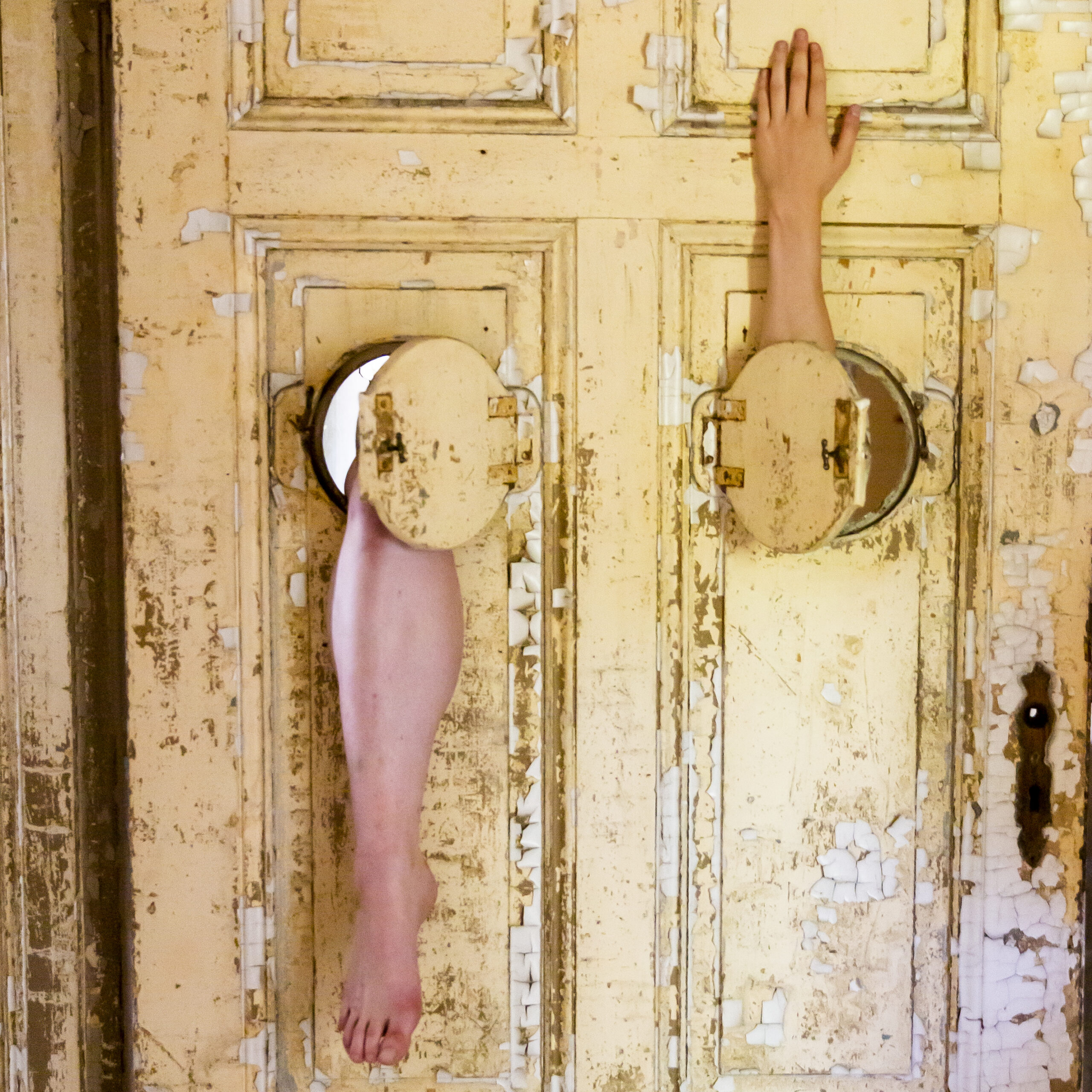 Young artist Merle Sommermeier hanging on door in an abandoned building, only with a visible hand and leg.